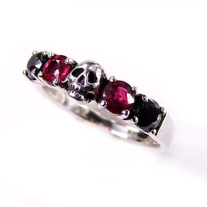 May include: A silver ring with a skull design and red and black gemstones.