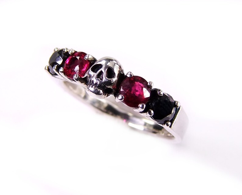 May include: A silver ring with a skull design and red and black gemstones.
