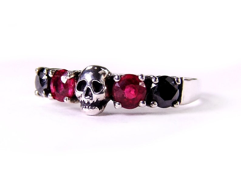 May include: A silver ring with a skull design and red and black gemstones.