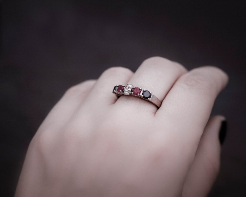 May include: A silver ring with a skull design and red and black gemstones.