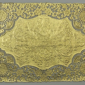 May include: Gold-colored lace doily with a floral design. The doily has a scalloped edge and a delicate, intricate pattern.