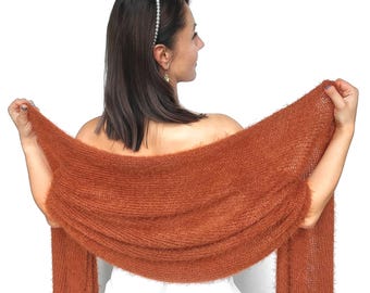 May include: A rust-colored, fluffy knit shawl. The shawl is held up, displaying its texture and drape. The material appears soft and warm. The image is set against a white background, highlighting the shawl's color and texture.