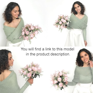 May include: A woman is wearing a sage green knitted shrug over a white skirt. She is holding a bouquet of pink roses. You will find a link to this model in the product description.
