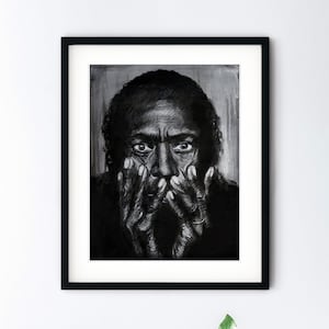 Puede incluir: Un dibujo en blanco y negro enmarcado de un rostro. La persona est&aacute; mirando hacia abajo con las manos cubri&eacute;ndose la cara. El dibujo est&aacute; en una pared blanca con una planta verde y una pila de libros delante.