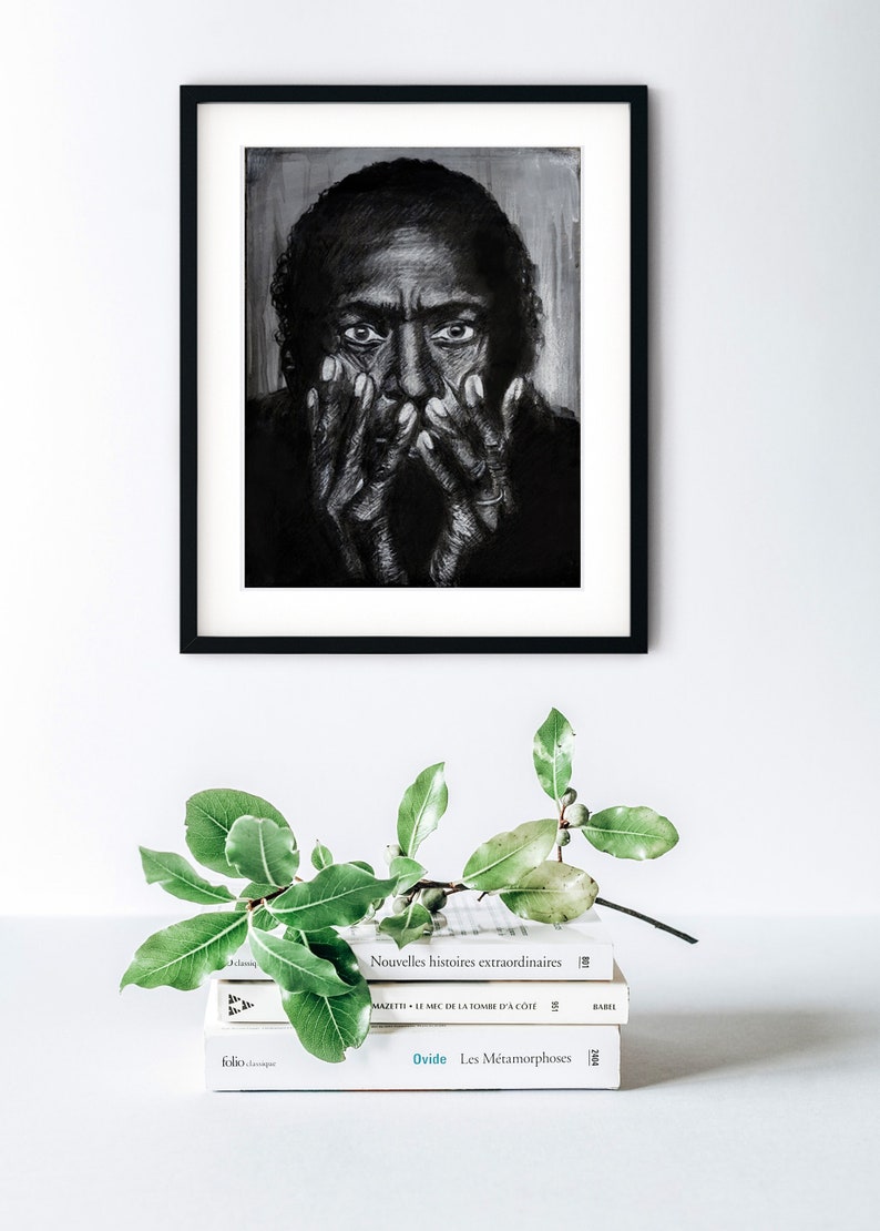 Puede incluir: Un dibujo en blanco y negro enmarcado de un rostro. La persona est&aacute; mirando hacia abajo con las manos cubri&eacute;ndose la cara. El dibujo est&aacute; en una pared blanca con una planta verde y una pila de libros delante.