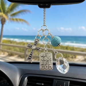 May include: A silver-toned car rearview mirror charm featuring a metal cross with embedded clear crystals, a rectangular metal tag engraved with the text LET GO! LET GOD, a textured light blue porous bead, and a clear faceted crystal pendant.