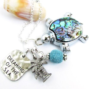 May include: Silver necklace with a charm of a turtle with a mother of pearl shell, a palm tree charm, a turquoise bead, and a silver charm with the text "Dreaming of the Sea".