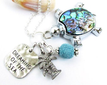 May include: Silver necklace with a charm of a turtle with a mother of pearl shell, a palm tree charm, a turquoise bead, and a silver charm with the text "Dreaming of the Sea".