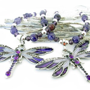 May include: Two dragonfly pendant necklaces. Each necklace features a silver-toned dragonfly pendant with purple and gray enamel wings and purple gemstone accents. The beaded necklace includes purple and silver beads.