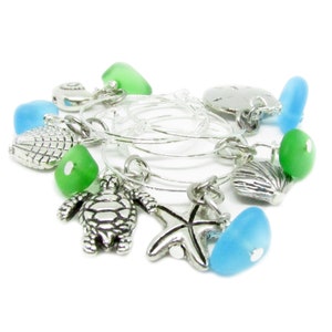 May include: Set of six silver wine glass charms with various sea-themed charms, including a starfish, seashell, turtle, and sea glass in shades of blue and green.