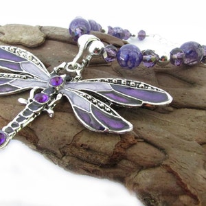 May include: A silver-toned dragonfly pendant necklace with purple enamel wings and purple gemstone accents. The necklace features a beaded strand of purple and silver beads. The dragonfly pendant is approximately 3 inches long.