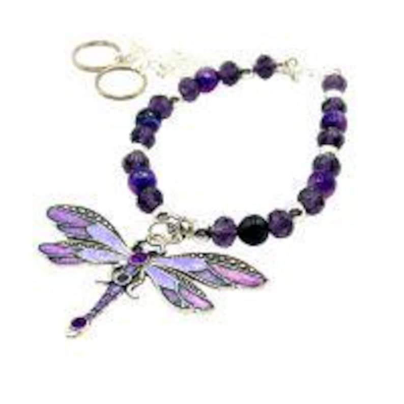 May include: A beaded bracelet with a dragonfly charm. The bracelet features purple and black beads, with a silver-toned clasp and a dragonfly pendant. The dragonfly has purple and silver details. Two silver-toned key rings are attached to the bracelet.