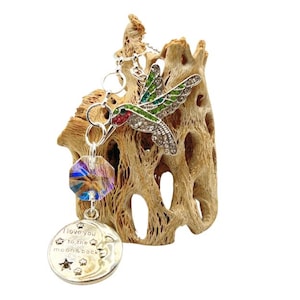 May include: A silver charm bracelet with a hummingbird charm, a crystal bead, and a round charm with the text "I love you to the moon & back".