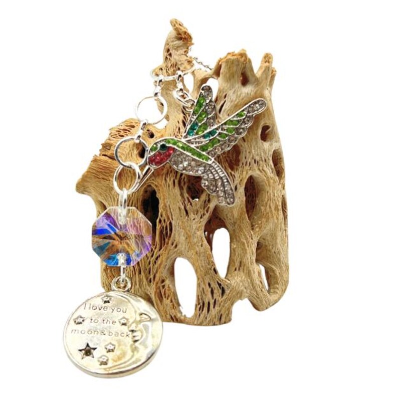 May include: A silver charm bracelet with a hummingbird charm, a crystal bead, and a round charm with the text "I love you to the moon & back".