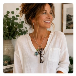 May include: A silver-toned metal necklace featuring a circular pendant ring that holds a turtle-shaped charm with an iridescent abalone shell inlay, a small green bead, and a pair of dark brown tortoiseshell-patterned eyeglasses hanging from it.