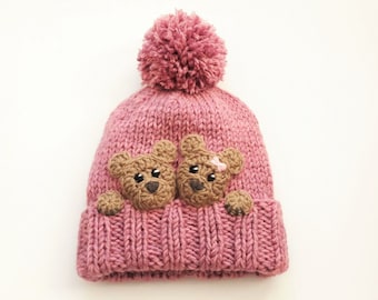 May include: Pink knitted hat with a fluffy pom pom on top and two brown bear appliques on the front.