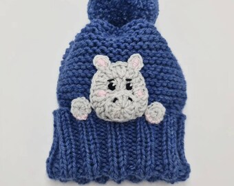 May include: Blue knitted hat with a gray hippopotamus appliqué and a blue pom-pom on top.