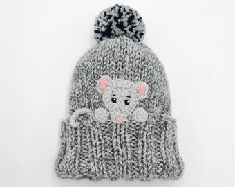 May include: Gray knitted beanie with a pom pom on top and a gray mouse peeking out from the front.