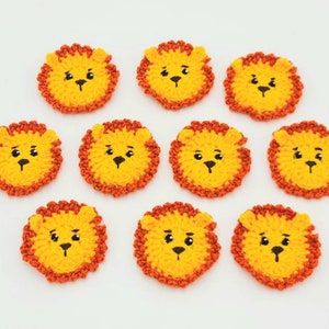 May include: Ten crocheted lion appliques in yellow and orange. Each applique has a black embroidered face with eyes, nose, and mouth.