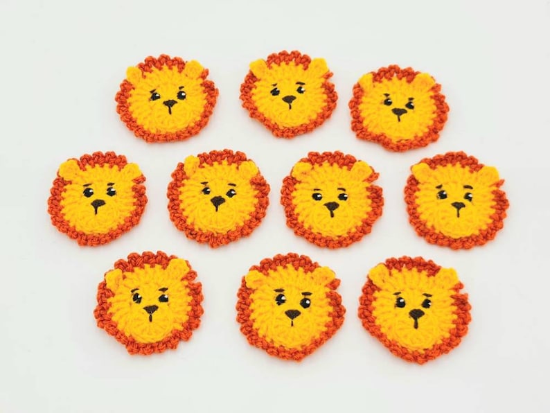 May include: Ten crocheted lion appliques in yellow and orange. Each applique has a black embroidered face with eyes, nose, and mouth.