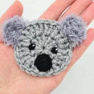 Puede incluir: Un koala de crochet gris con ojos y nariz negros. El koala tiene orejas grises y peludas.
