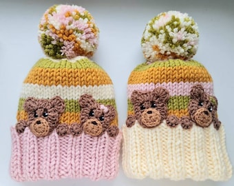 May include: Two knitted hats with pom-poms, one pink and one cream, both with brown bear appliques and stripes of green, yellow, and white.