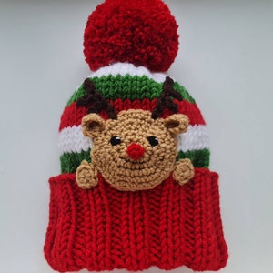 May include: Red and green striped knit hat with a white stripe and a brown reindeer face with a red nose. The hat has a red pom-pom on top.
