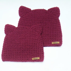 May include: Two burgundy crocheted hats with ear flaps and a brown leather tag that says "2mice" on each hat.