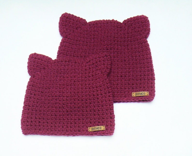 May include: Two burgundy crocheted hats with ear flaps and a brown leather tag that says "2mice" on each hat.
