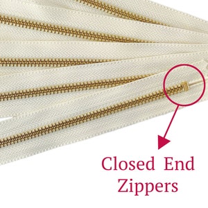 May include: A close-up of several white zipper tapes with gold metal teeth. The zipper ends are closed, indicating they are closed-end zippers.