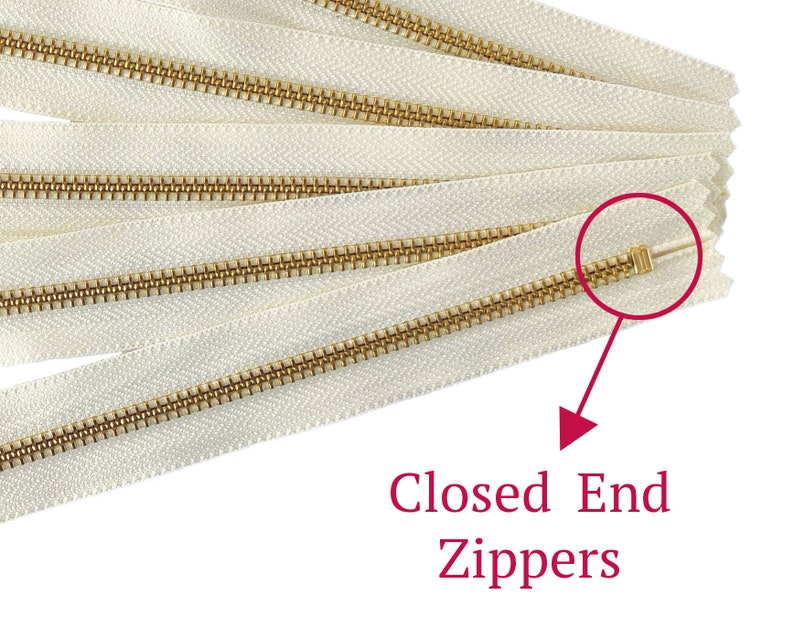 May include: A close-up of several white zipper tapes with gold metal teeth. The zipper ends are closed, indicating they are closed-end zippers.