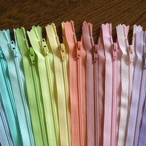 Puede incluir: Un surtido arco&iacute;ris de cierres de cremallera en varios colores pastel, incluyendo azul claro, verde, amarillo, naranja, rosa y morado.
