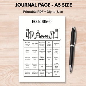May include: A black and white printable "Book Bingo" game sheet with a bookshelf graphic. The sheet includes various book-related prompts. A black pen rests on the wooden surface next to the sheet. The text "JOURNAL PAGE - A5 SIZE" is at the top.