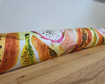 May include: A cylindrical fabric door draft stopper featuring a vibrant watercolor pattern of tropical fruits. The design includes papaya, dragon fruit, and bananas in shades of orange, yellow, and pink. The stopper rests on a wooden surface.