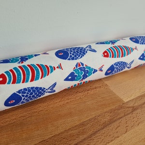 May include: White doorstop with a blue and red fish pattern. The doorstop is cylindrical and has a white background with blue and red fish printed on it.