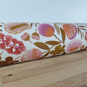 Könnte beinhalten: Gerollter Stoff mit floralem Muster auf cremefarbenem Hintergrund. Das Design umfasst orange, rosa und lila Blumen mit braunen Stielen und Blättern. Der Stoff liegt auf einer Holzoberfläche.