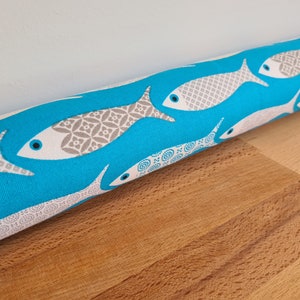 May include: A turquoise blue doorstop with a white and gray fish pattern. The doorstop is made of fabric and is approximately 10 inches long.