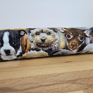 Puede incluir: Tela con un patrón repetido de cachorros adorables. Los cachorros tienen varios colores de pelaje, incluyendo blanco y negro, marrón y beige. La tela se utiliza probablemente para proyectos de manualidades o decoración del hogar.