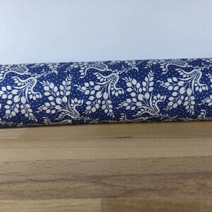 May include: Rolled fabric with a navy blue background and a white floral pattern. The design features stylized leaves and dots, creating a classic look. The fabric is rolled up, showing the pattern's repeat.
