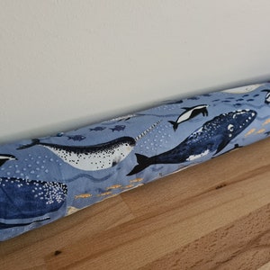 May include: A blue and white doorstop with a whale, narwhal, and fish pattern. The doorstop is lying on a wooden floor.