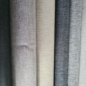 May include: Close-up of six fabric swatches in various shades of gray, from black to light gray. The fabric has a textured weave.