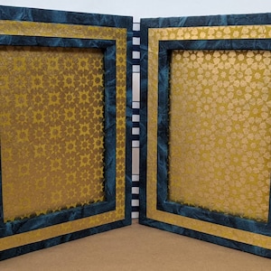 May include: Two blue picture frames with gold trim and a gold star pattern inside. The frames are open and facing each other.