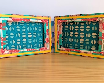 May include: Two rectangular picture frames with colorful patterned paper. The frames have a teal background with a white and tan pattern. The frames are trimmed with yellow, red, and green patterned paper.