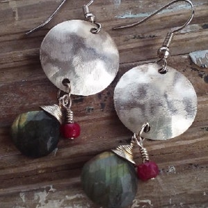 Puede incluir: Pendientes de plata con un disco redondo martillado y un colgante de piedra verde. Los pendientes tienen un acento de cuentas rojas.