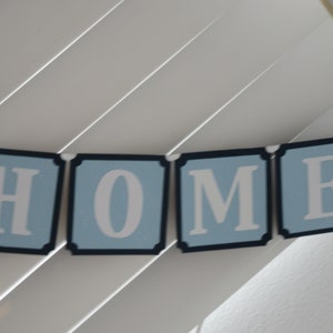May include: A blue and white banner with the word "HOME" spelled out in white letters on a light blue background. Each letter is on a separate banner section with a black border.