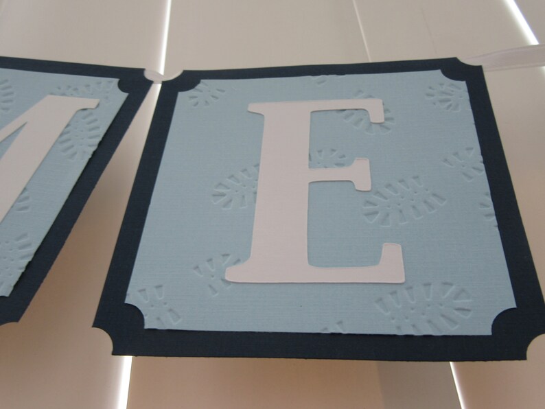 May include: A blue banner with a white letter "E" on it. The banner has a navy blue border and a white snowflake pattern.