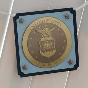 May include: A blue and black banner with a gold seal featuring the United States Air Force emblem. The seal has a bald eagle with outstretched wings and a shield with a star and lightning bolts. The text "UNITED STATES AIR FORCE" is written around the seal.