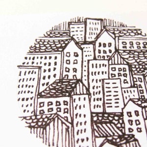 May include: Black and white ink drawing of a city skyline with multiple buildings, all with windows and roofs. The drawing is in a circle shape.