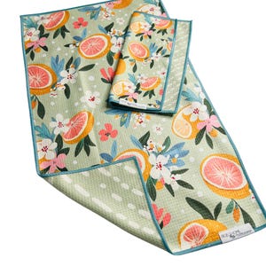 May include: A set of three kitchen towels with a light green background and a vibrant citrus fruit and floral pattern. The design features orange and pink grapefruit slices, white flowers, and blue leaves. The towels have a teal border.