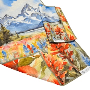May include: A set of three microfiber towels with a watercolor landscape design. The towels feature a mountain range, colorful wildflowers, and a blue sky. The towels are in shades of blue, orange, yellow, and green.
